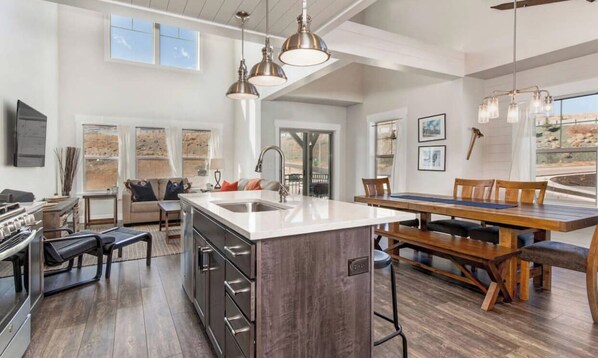A spacious kitchen with a central island, a dining area with a wooden table, and a large window offering a view. - Moose Mgmt at Wasatch Springs 13804: Free Bus Routes-Garage Parking-Fast WiFi (Park City)
