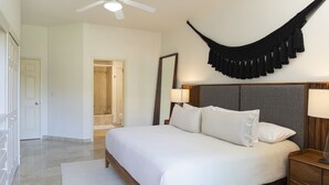 A hotel room with a large bed, a ceiling fan, a hammock, and a wooden nightstand with a lamp.