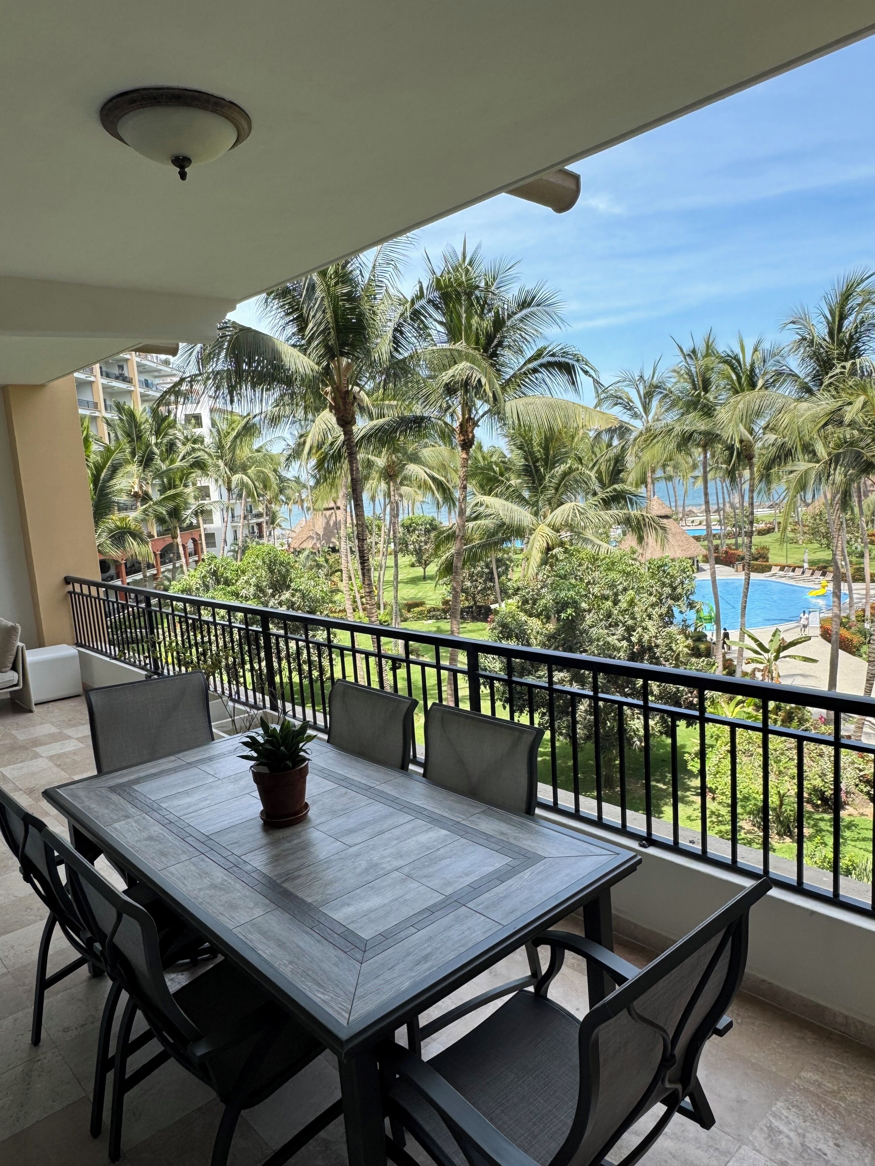 Un balcon avec une table et des chaises, donnant sur une piscine et des palmiers.