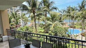 A balcony with a table and chairs, overlooking a pool and palm trees.