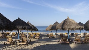 A beach with rows of sun loungers and thatched umbrellas.