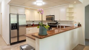 A modern kitchen with white cabinets, stainless steel appliances, a granite countertop, and a potted orchid.