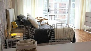 A modern living room with a sofa, a coffee table, and a view of a cityscape through large windows. - Cozy Studio 7 Palermo Soho/ Balcony/Pool/Sum/AA. (Buenos Aires)