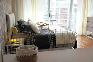 Un salon moderne avec un canapé, une table basse et une vue sur le paysage urbain, visible à travers de grandes fenêtres.