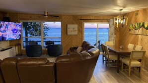 Una sala de estar acogedora con televisor grande, sofás de cuero, comedor y vistas al mar.