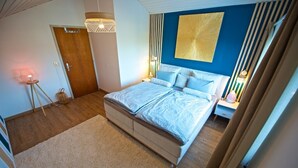 Une chambre à coucher comprenant un lit, une table de chevet, une lampe et un mur orné d’un motif géométrique.