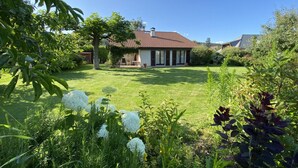Une maison avec un toit recouvert de tuiles rouges, entourée d’une pelouse bien entretenue et de diverses plantes.