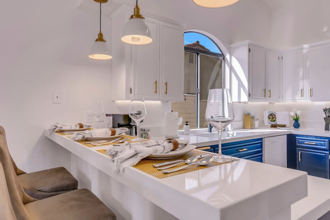 Een moderne keuken met witte kastjes, een centraal eiland met een eettafel en hangende lampen.