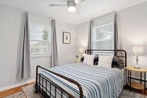 A bedroom with a bed, two bedside tables, a ceiling fan, and a window with curtains. - Cozy Carriage Haus Close To Everything - Unit A (Cheyenne)