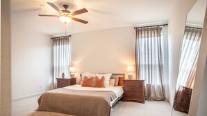 Ein Schlafzimmer mit einem Bett, zwei Nachttischen, einem Deckenventilator und transparenten Vorhängen.