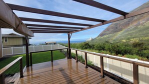 Un muelle de madera con un pérgola, una valla blanca y vistas a un paisaje verde y al océano.