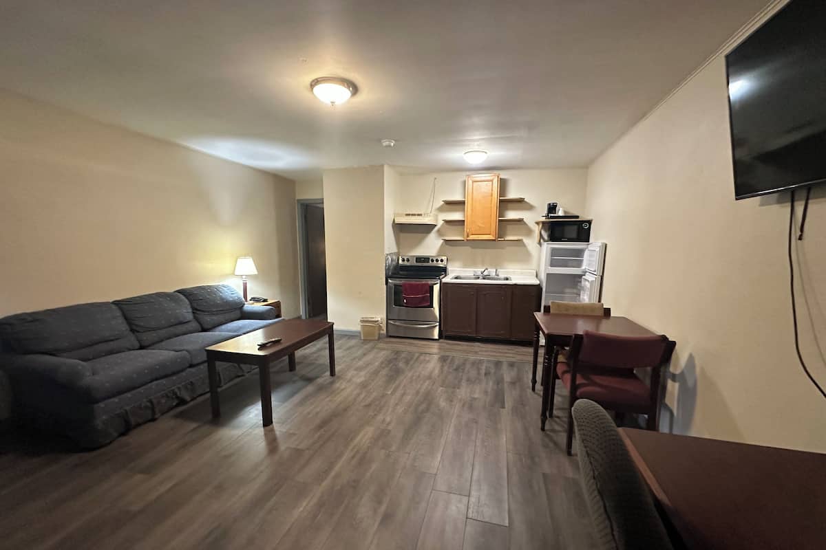 Un espacio habitable compacto con sofá, una mesita, kitchenette y televisor montado en la pared.