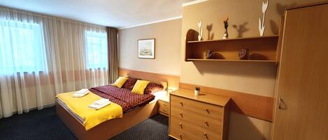 A hotel room with a bed, a dresser, a nightstand, and a shelf with decorative items.