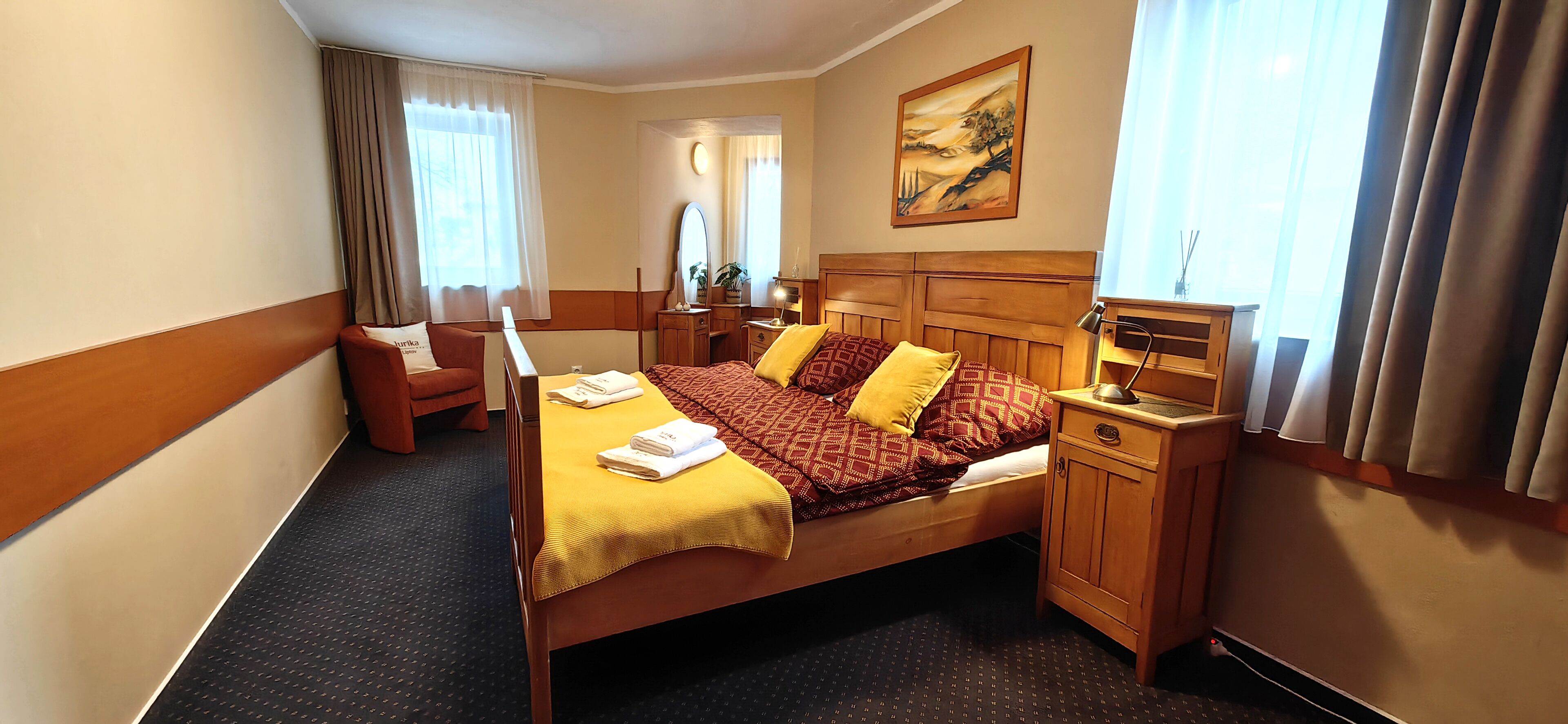 A hotel room with a bed, bedside table, lamp, chair, and a painting on the wall.