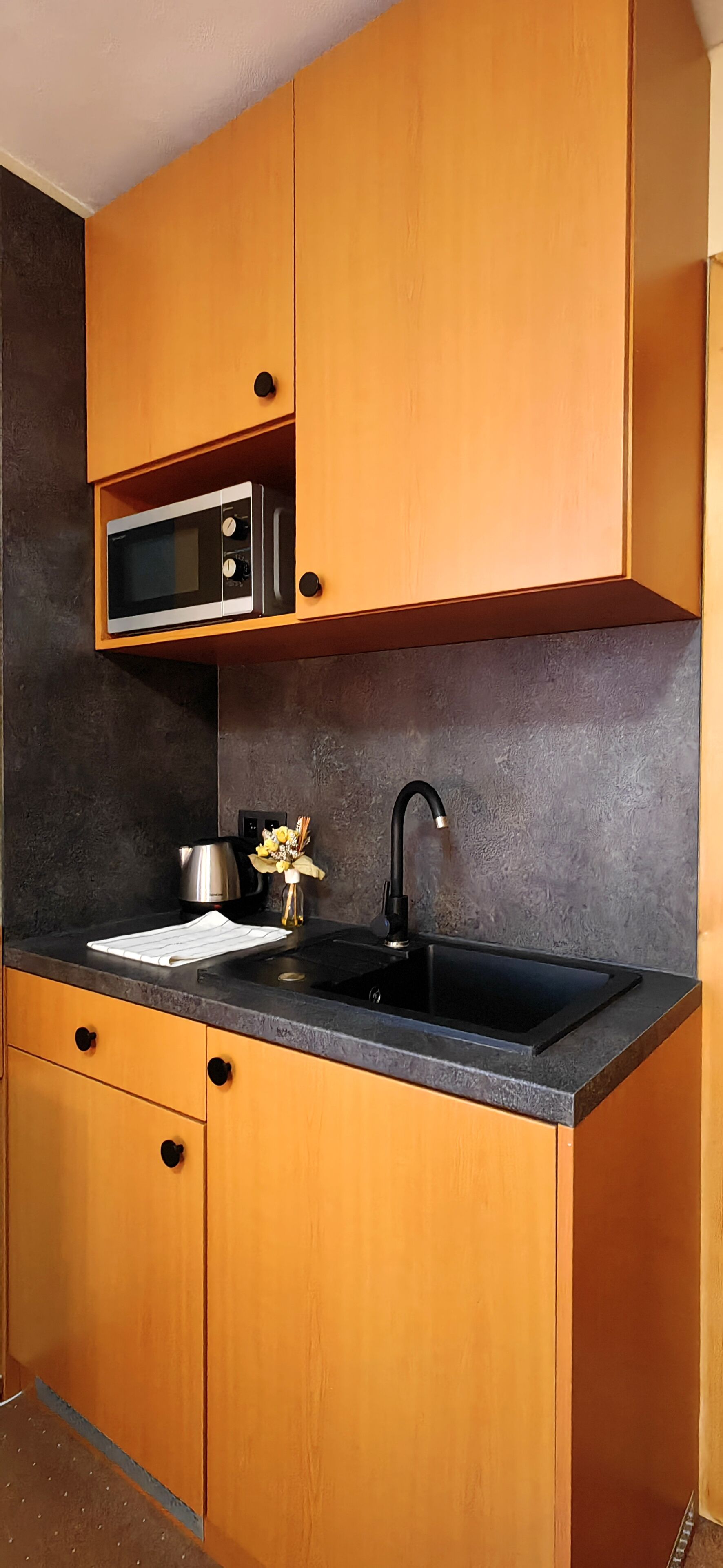 Una cocina con armarios de madera, encimera negra, hervidor de acero inoxidable y grifo negro.