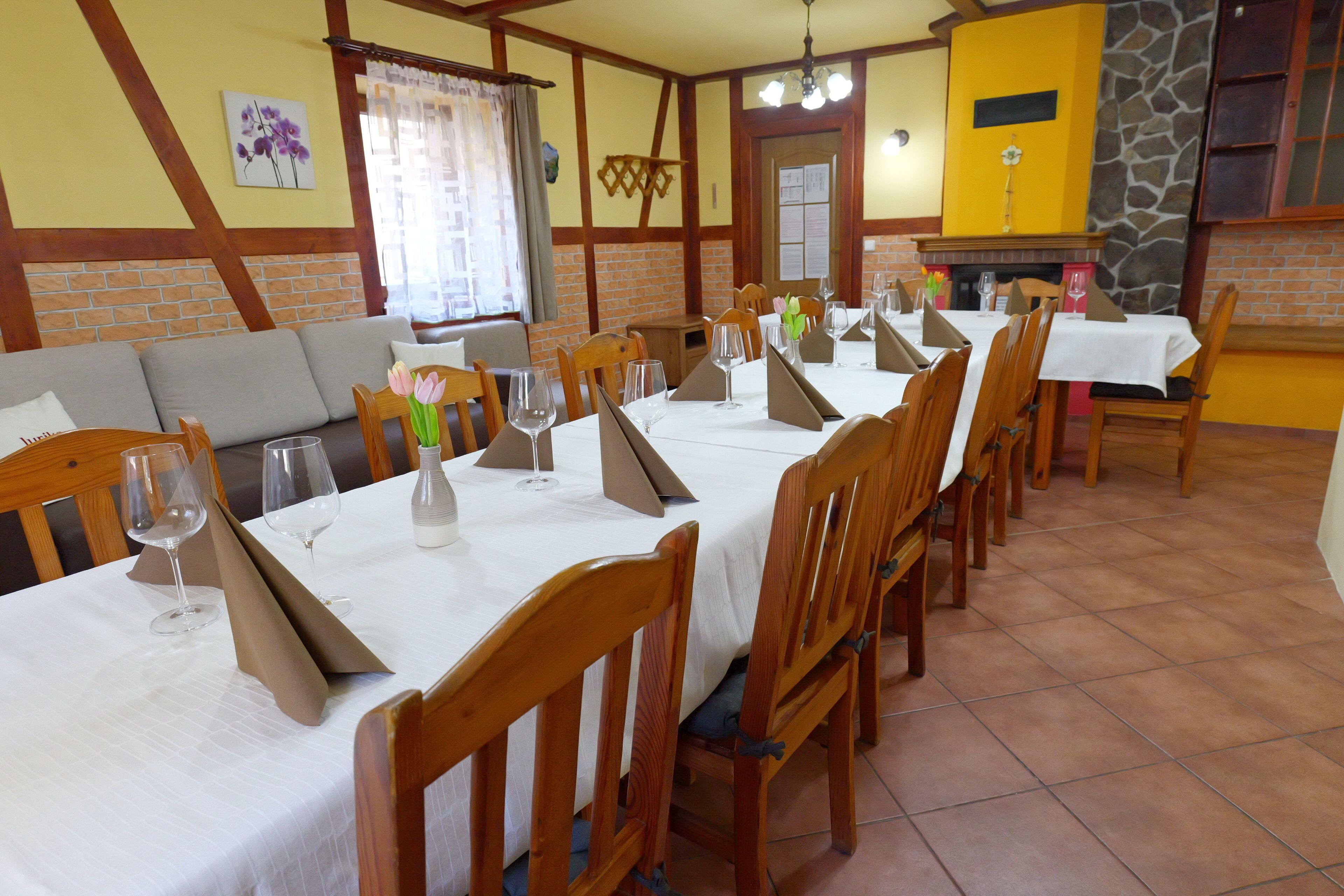 Un comedor con varias mesas dispuestas para invitados, sillas de madera y una pared de ladrillo con chimenea.
