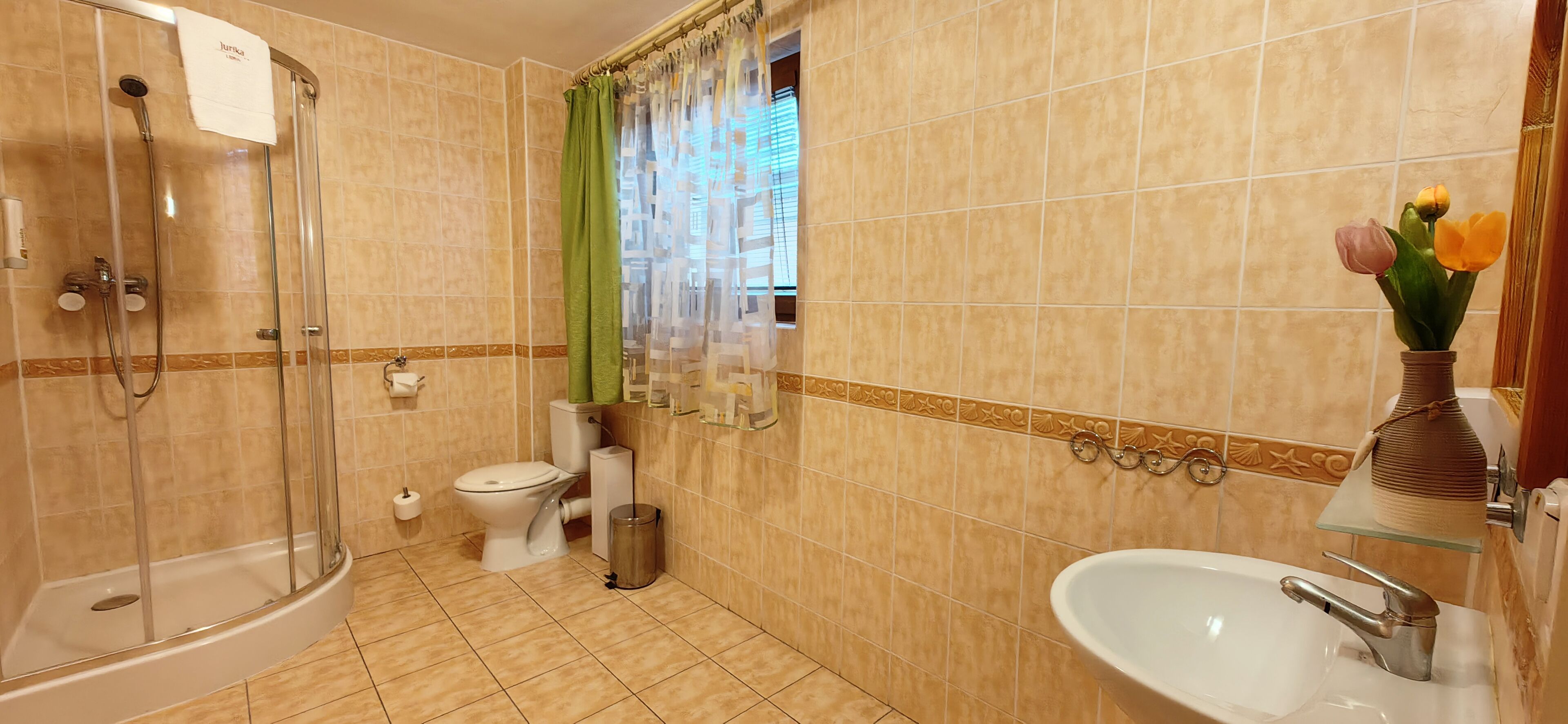 A bathroom with a shower, toilet, sink, and a vase with flowers.