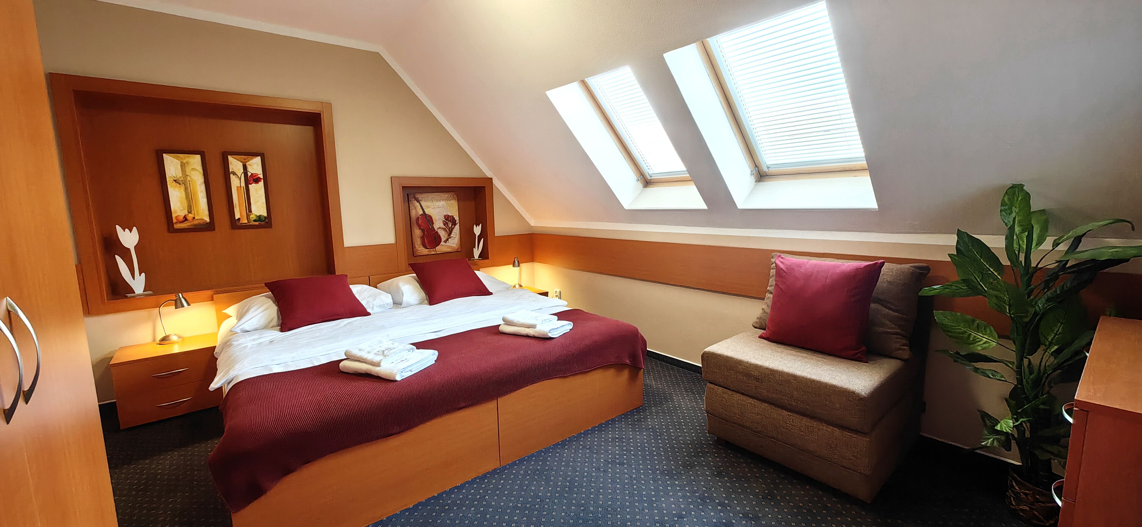 A hotel room with a large bed, a sofa, a desk, and a skylight.