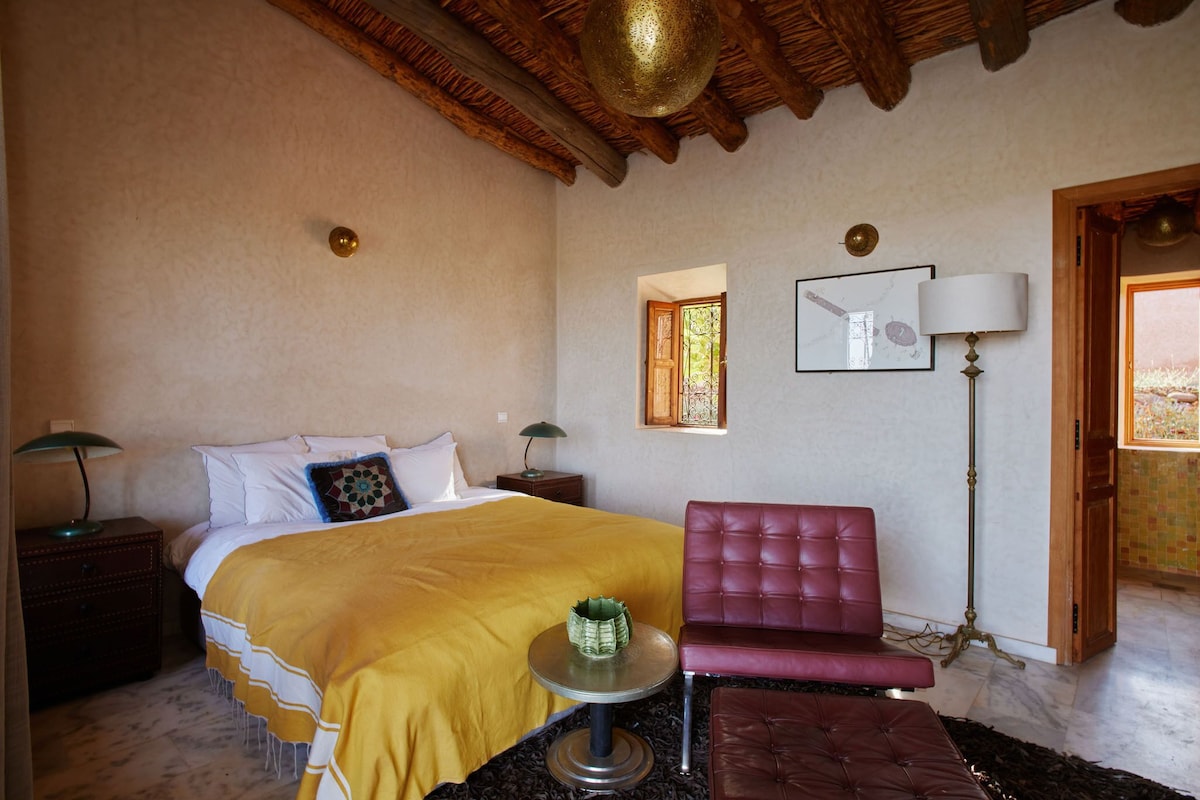 Un dormitorio con una cama, una silla roja, una lámpara y una mesita.