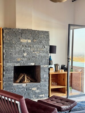 A modern living room with a stone fireplace, leather furniture, and a view through a glass door. - dar imiri (Ghmate)