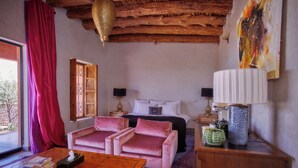 Quarto acolhedor com cama, duas mesas de cabeceira, uma mesa de centro de madeira, um sofá rosa e uma janela grande com cortinas vermelhas.