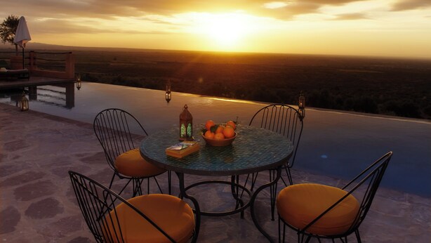 Vista do pôr do sol a partir de um terraço com uma mesa redonda e cadeiras, uma tigela de frutas e lanternas.