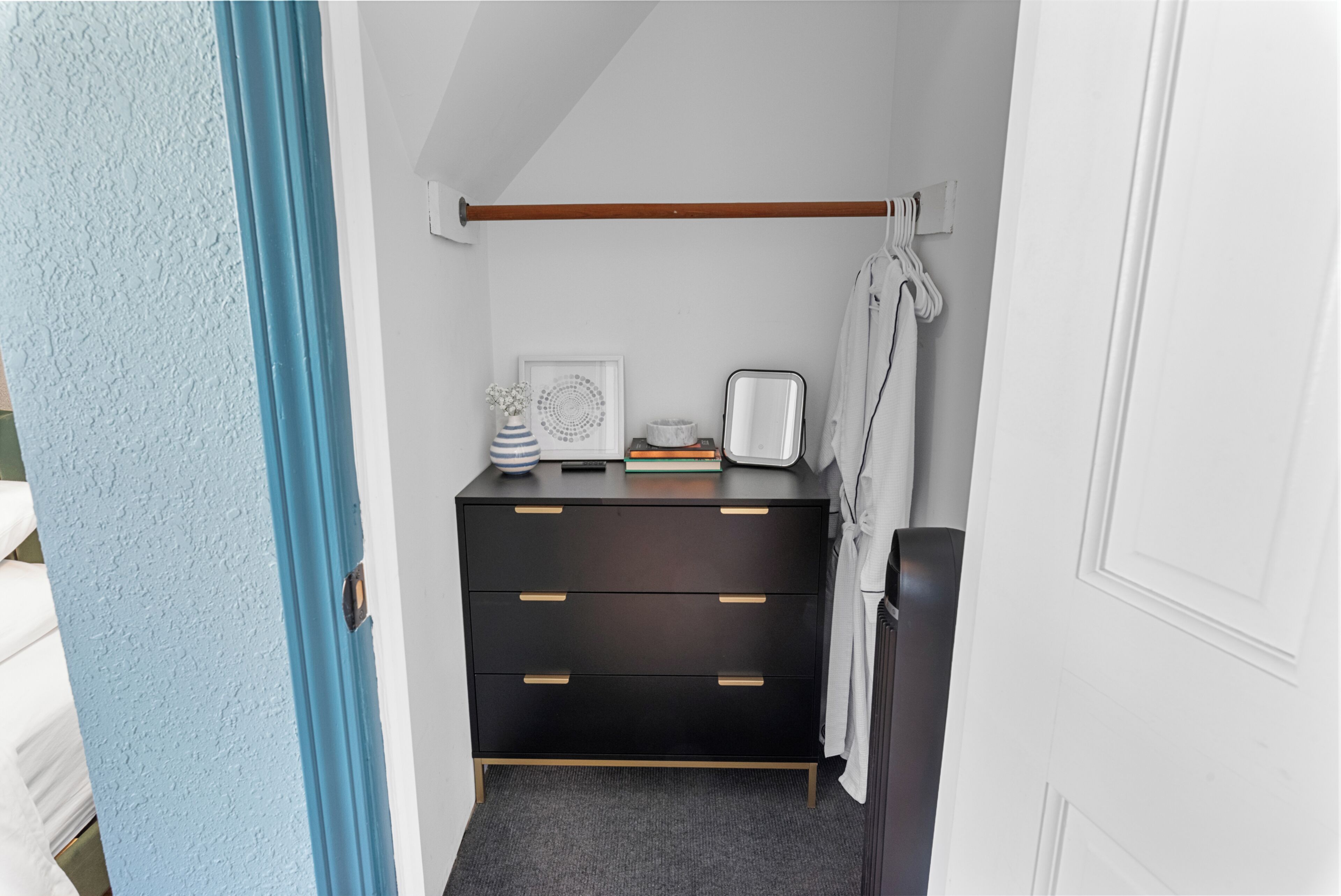 Un dormitorio compacto con un aparador negro, una mesita de noche pequeña, un cuadro enmarco y un radiador blanco.