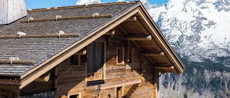 A wooden mountain cabin with a steep roof, wooden beams, and a view of snow-capped mountains.