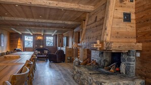 Un intérieur rustique avec des éléments en bois, notamment une longue table à manger, une cheminée en pierre et des murs en bois.