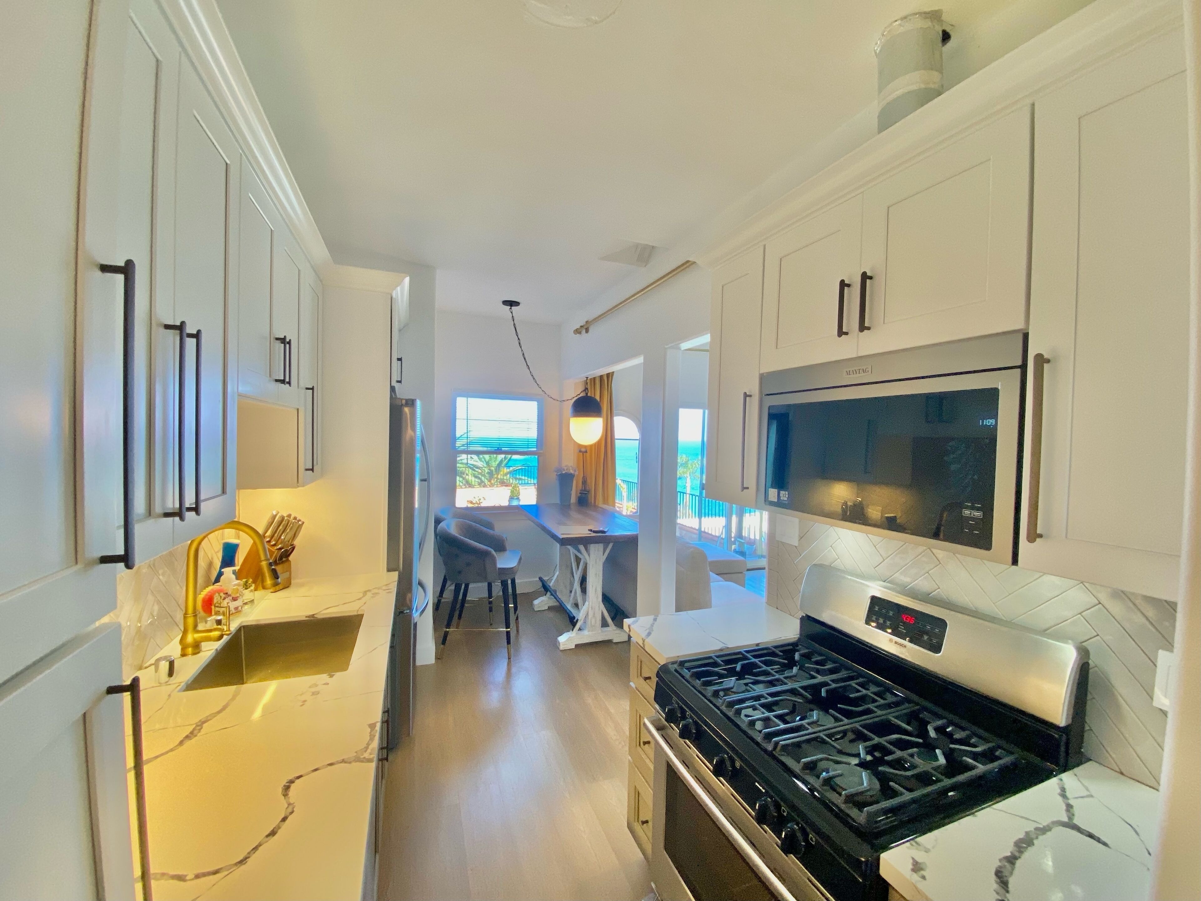 A modern kitchen with white cabinetry, a stainless steel stove, and a large window overlooking a scenic view.