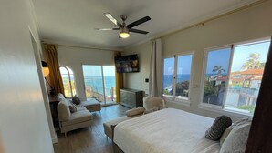 A bedroom with a large bed, a sofa, a TV, and a balcony with a view of the ocean. - Penthouse with Unobstructed Views! (San Pedro)