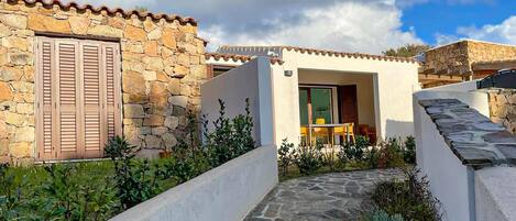 A stone building with a tiled roof, a doorway, and a small outdoor seating area.