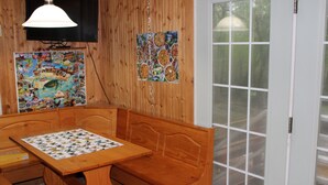 Un comedor de madera con una mesa y bancos, un televisor montado en la pared y una puerta con paneles de vidrio.