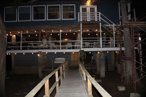 A wooden deck leading to a building with a balcony, surrounded by trees and a metal scaffold structure.