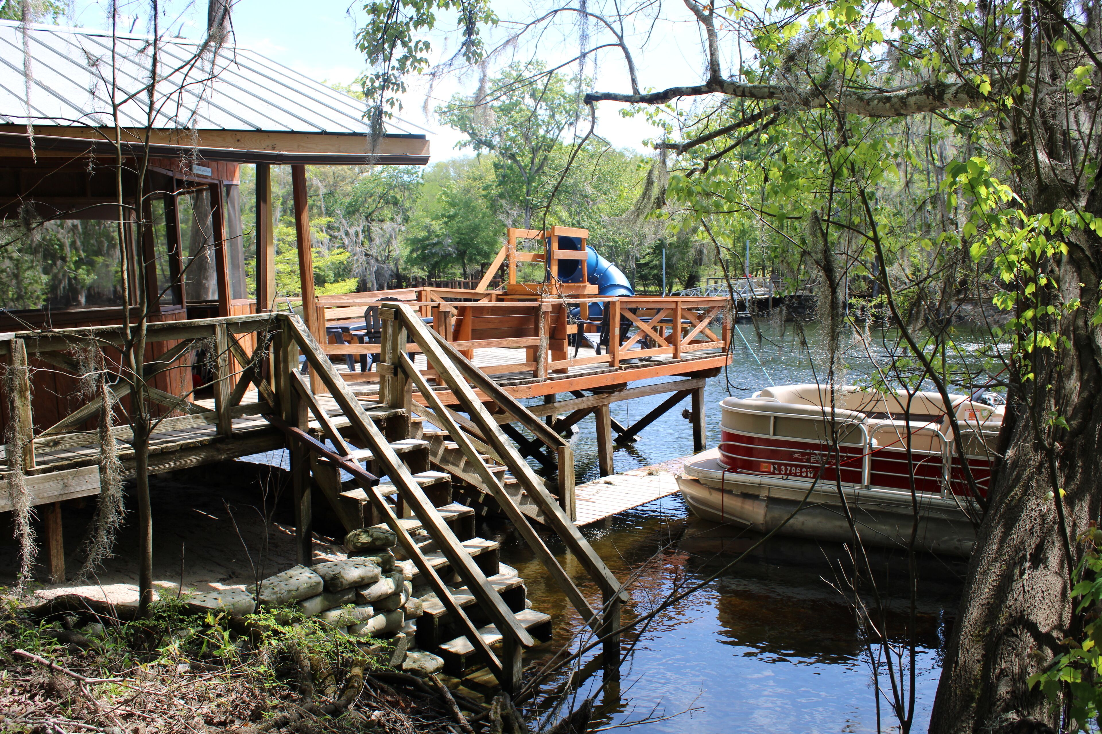 A wooden dock with a boat, a wooden staircase, and a building with a metal roof.