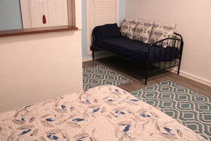 A bedroom with a bed, a window with blinds, and patterned rugs.