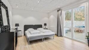Ein modernes Schlafzimmer mit einem großen Bett, zwei Nachttischlampen, einem Spiegel und einer Glasschiebetür, die zu einem Außenbereich führt.