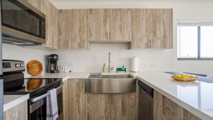 Een moderne keuken met houten kastjes, roestvrijstalen apparatuur, een grote spoelbak en een raam met jaloezieën.
