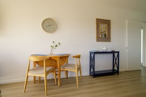 A room with a wooden desk, two chairs, a small table with a vase, a clock, and a mirror on the wall.