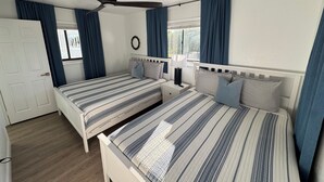 Een slaapkamer met twee bedden, een plafondventilator, een raam met gordijnen en een deur.