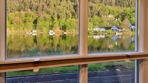 A view through a window of a lake with boats, a forested hillside, and houses in the background.