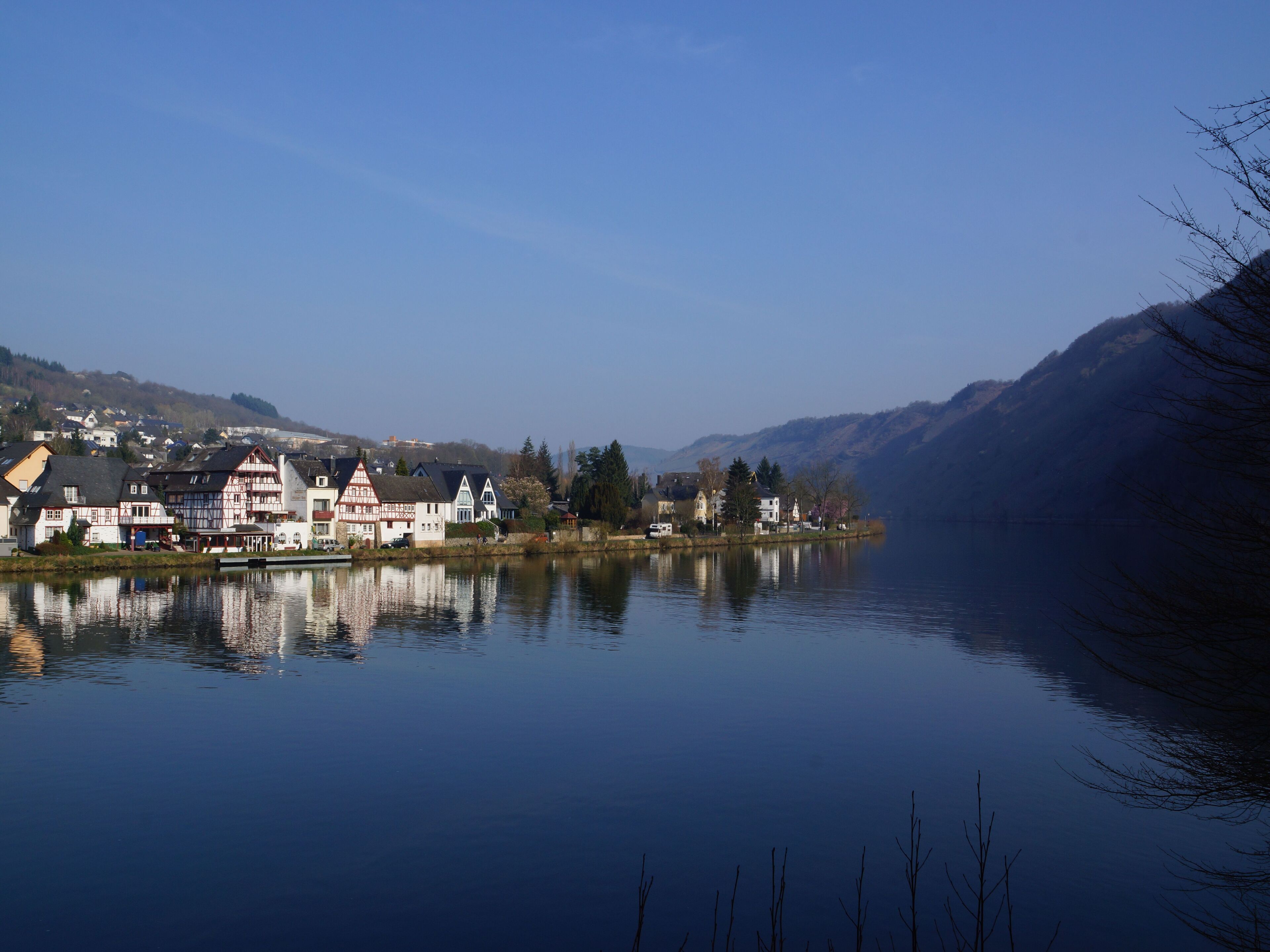 Un village au bord d’un lac, avec des bâtiments traditionnels, une eau calme et des collines en arrière-plan.