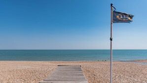 A wooden pier leading to a pebble beach with a flag on a flagpole. - Southbeach by Bloom Stays -  a holiday let that sleeps 4 guests  in 1 bedroom (Hythe)