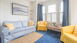 A living room with a striped sofa, a yellow armchair, a blue sofa, and a wooden coffee table with a vase of flowers. - Southbeach by Bloom Stays -  a holiday let that sleeps 4 guests  in 1 bedroom (Hythe)