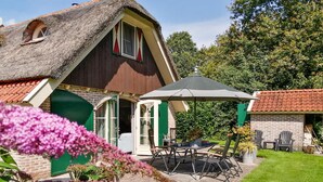 A house with a thatched roof, a patio with a table and chairs, and a garden with flowers.
