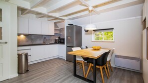 A modern kitchen with white cabinets, a stainless steel refrigerator, and a dining area with a wooden table and chairs.