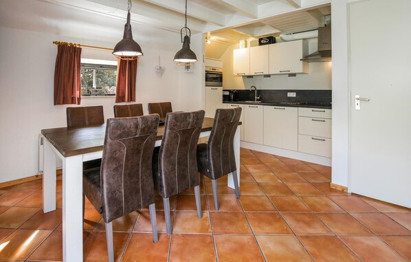 A dining area with a table and chairs, a kitchen with white cabinets and a stove, and a window with curtains.