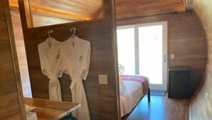 A compact room with a bed, a small kitchenette, and a wooden ceiling. - Cabernet Cabin (Seguin)