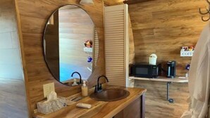 A compact bathroom with a wooden vanity, a sink, a mirror, a towel rack, and a small refrigerator. - Cabernet Cabin (Seguin)