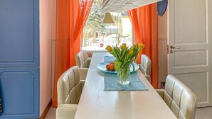 Un coin repas avec une table blanche, des rideaux orange et un vase rempli de fleurs jaunes.